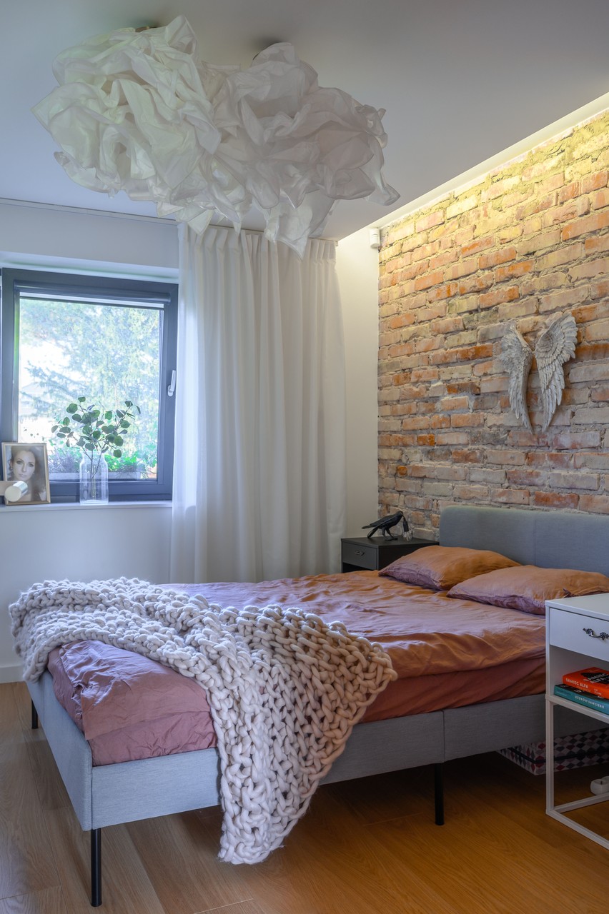 Przytulna sypialnia z czerwoną cegłą i designerską lampą.