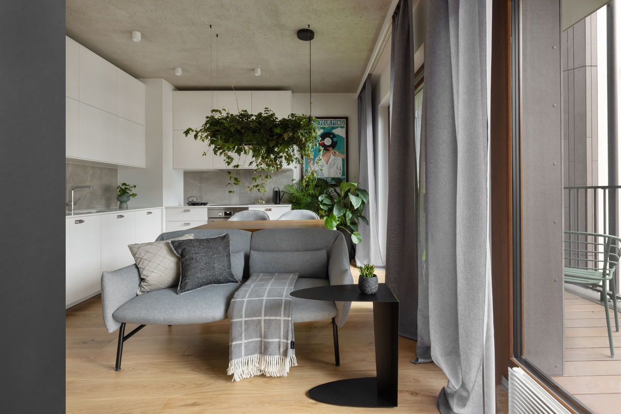Nowoczesny salon z roślinami, szarą sofą i stylowym stolikiem.