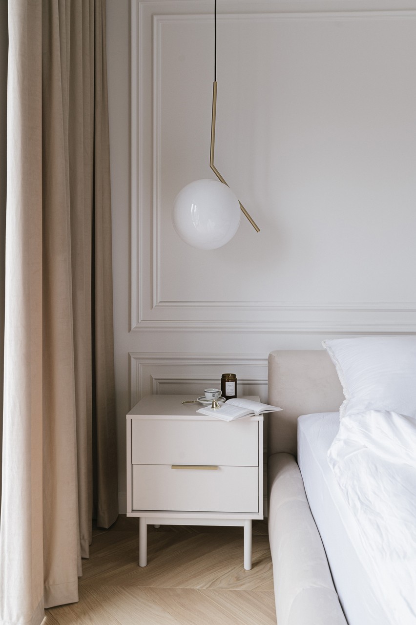 Minimalistyczna sypialnia z designerską lampą i nowoczesną szafką.