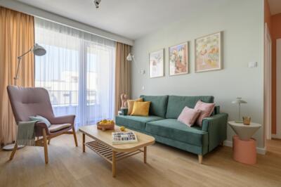 Przytulny salon z zieloną sofą i pastelowymi dodatkami.