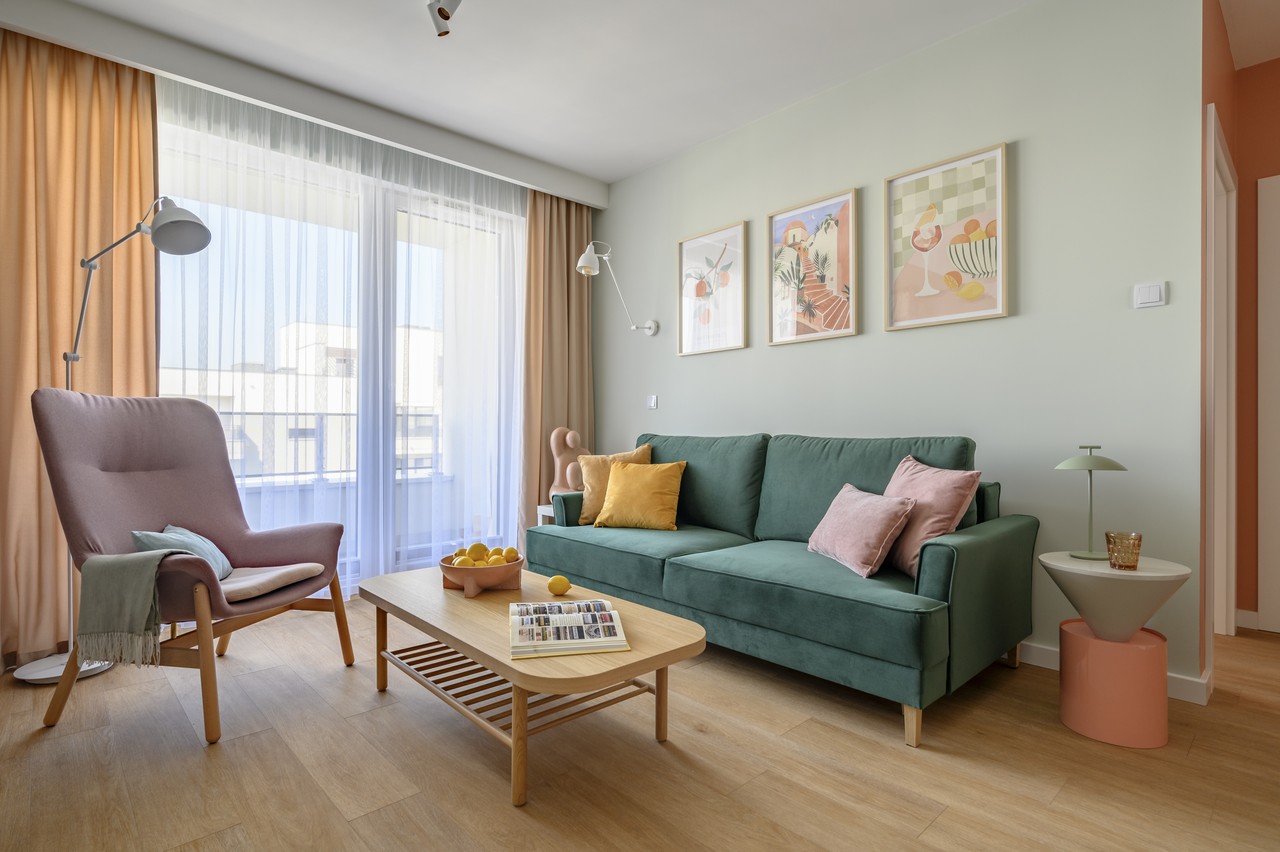 Przytulny salon z zieloną sofą i pastelowymi dodatkami.