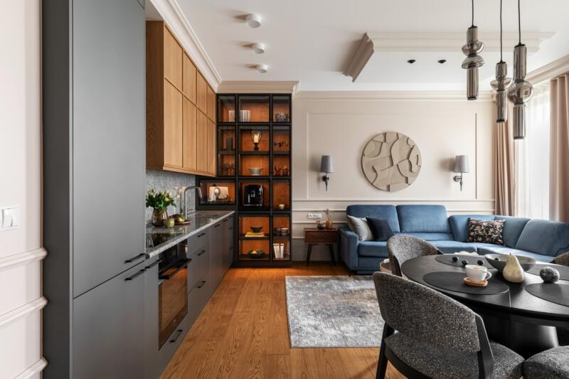 Elegancki salon z kuchnią, drewniane akcenty i niebieska sofa.