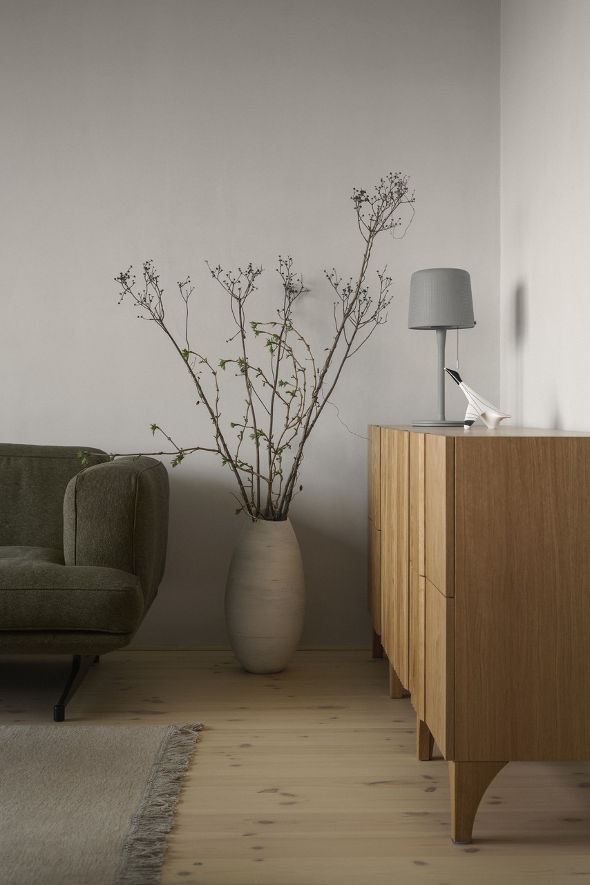Minimalistyczny salon z zieloną sofą i drewnianą komodą.