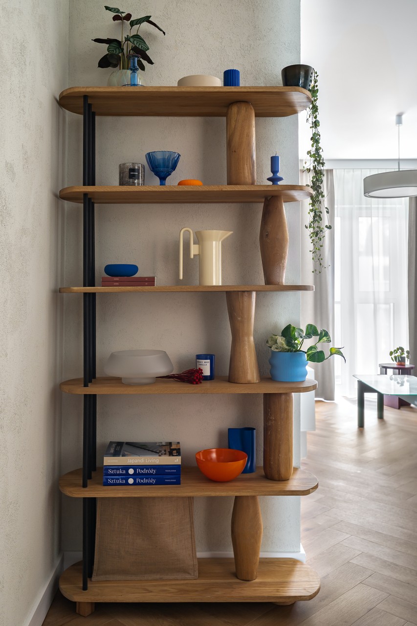 Regał z designerskimi ozdobami i roślinami w eleganckim wnętrzu.