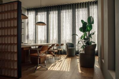 Elegancki salon z dużymi oknami, zielenią i drewnianym stołem.