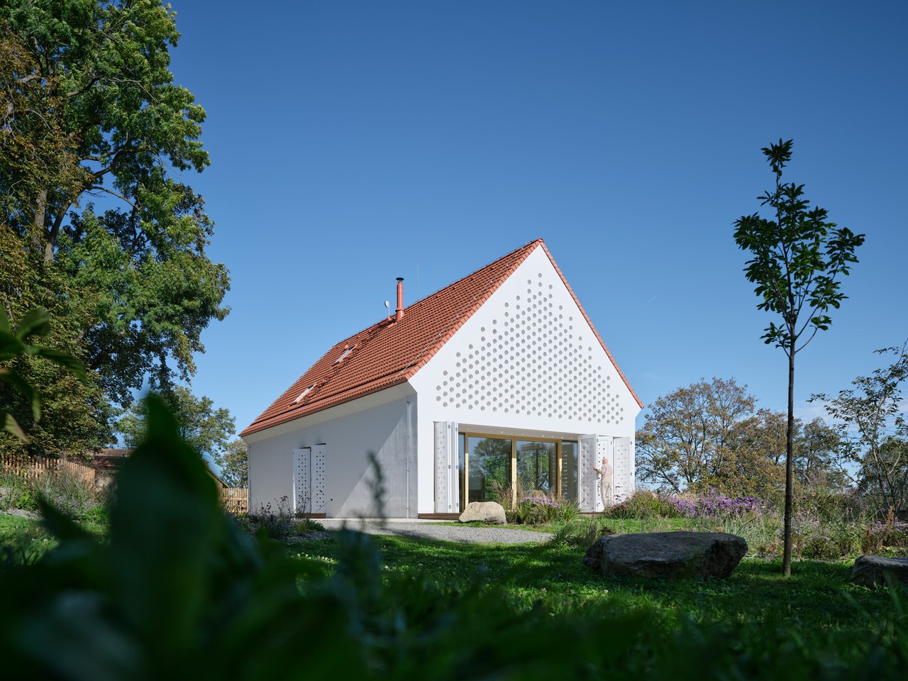 Biały dom z czerwoną dachówką w malowniczym krajobrazie.