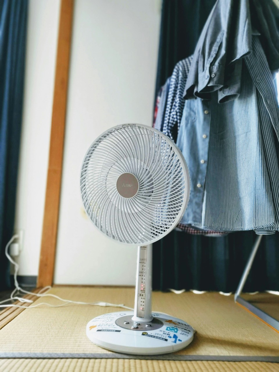 Wentylator na podłodze tatami, obok stoją suszące się ubrania.