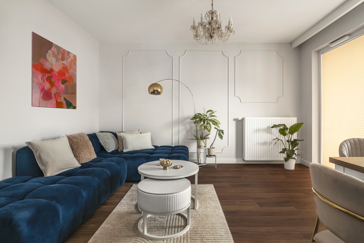 Elegancki salon z granatową sofą i złotą lampą.