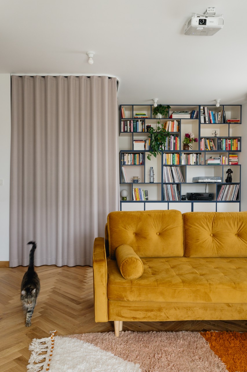 Żółta sofa, drewniana podłoga, stylowa biblioteka, zasłony i kot.