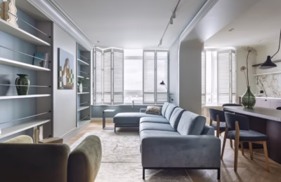 Elegancki salon z szarym sofą i dużymi oknami.