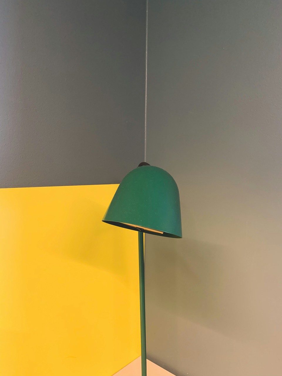 Zielona lampa na tle żółto-szarej ściany, nowoczesny design.