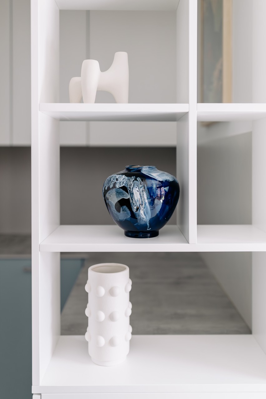 Minimalistyczna półka z elegancką ceramiką i designerską wazą.