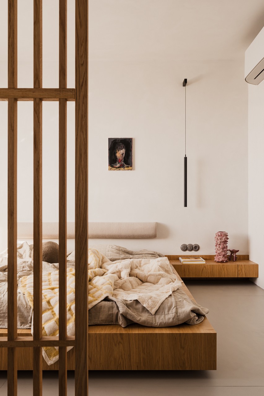 Minimalistyczna sypialnia z drewnianym łóżkiem i designerskim oświetleniem.