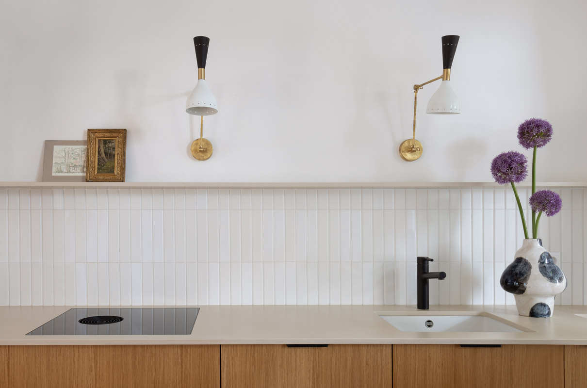 Minimalistyczna kuchnia z designerskimi lampami i wazonem kwiatów.
