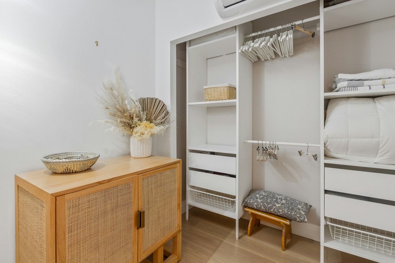 Minimalistyczna garderoba z białymi półkami i stylową komodą z wikliny.