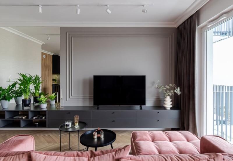 Modern living room with pink sofa and plants against a grey wall.