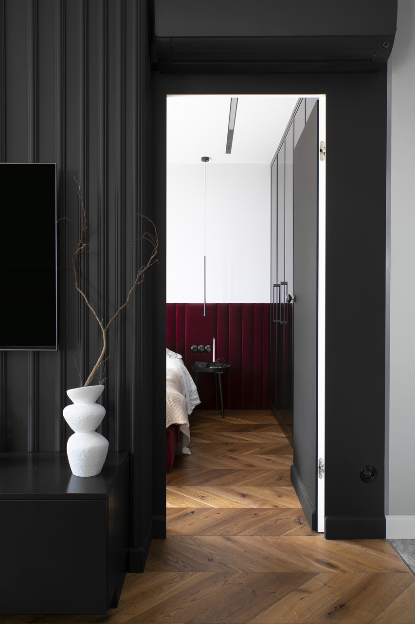 Modern bedroom with wooden floor and burgundy headboard.