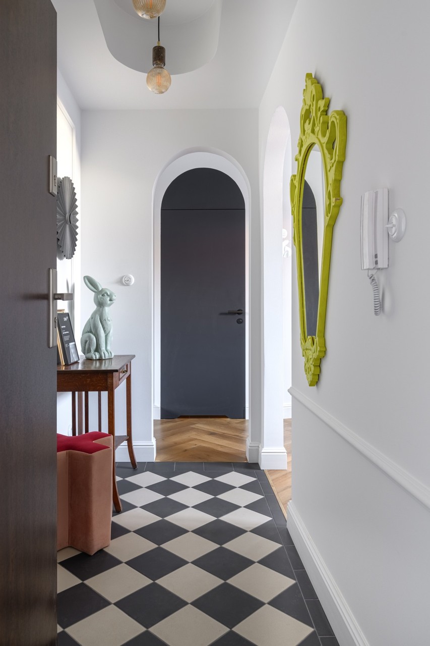 A corridor with a mirror in an ornate frame and black and white flooring.