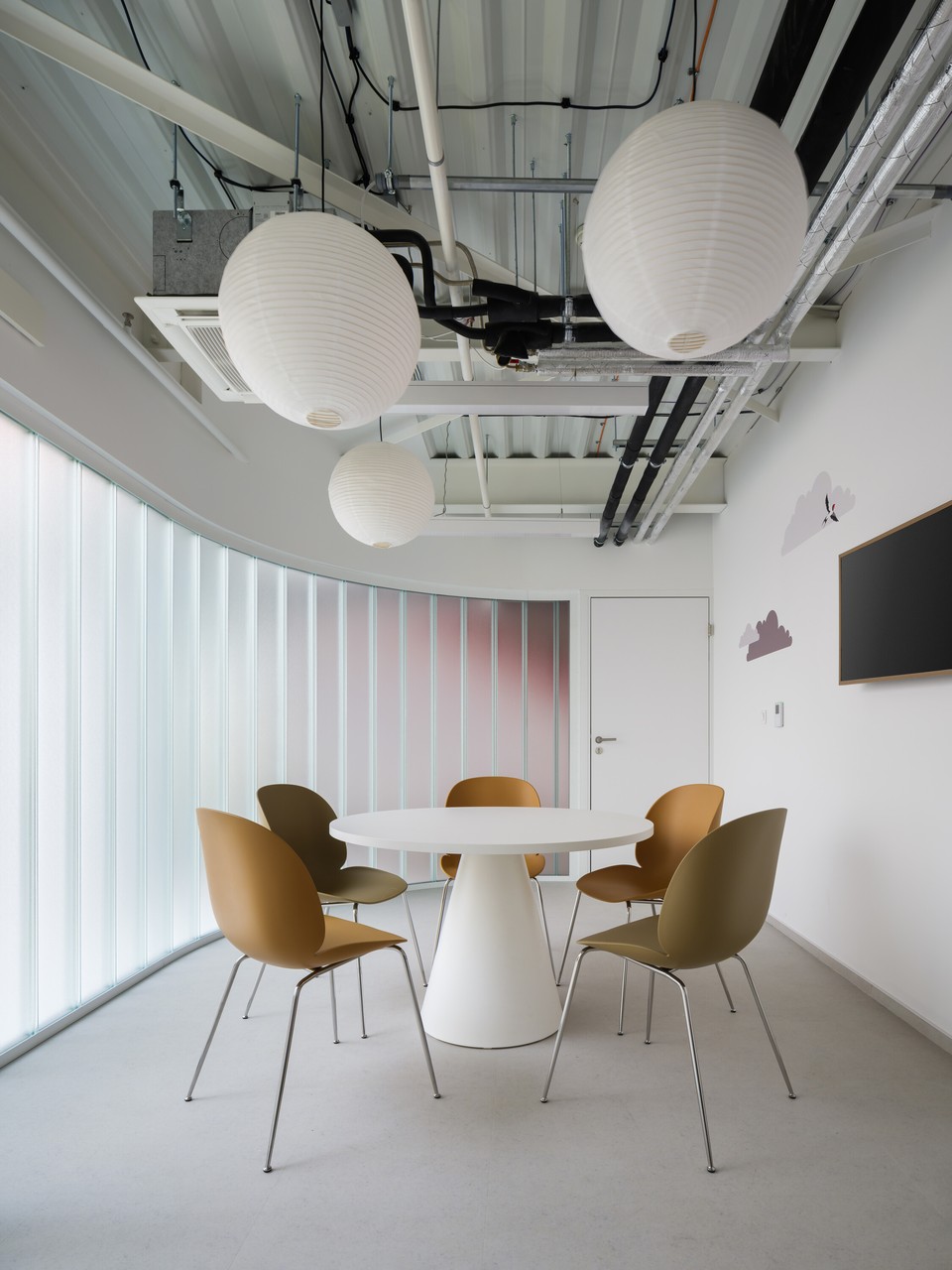 Minimalistyczna sala z okrągłym stołem i designerskimi krzesłami.