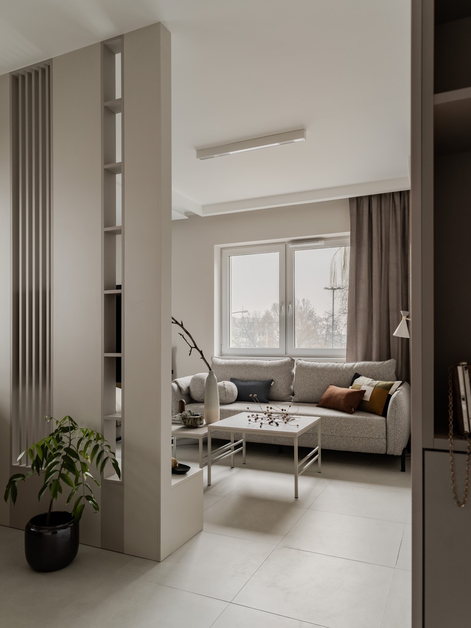 Nowoczesny salon z jasną sofą i dużym oknem, minimalistyczny wystrój.