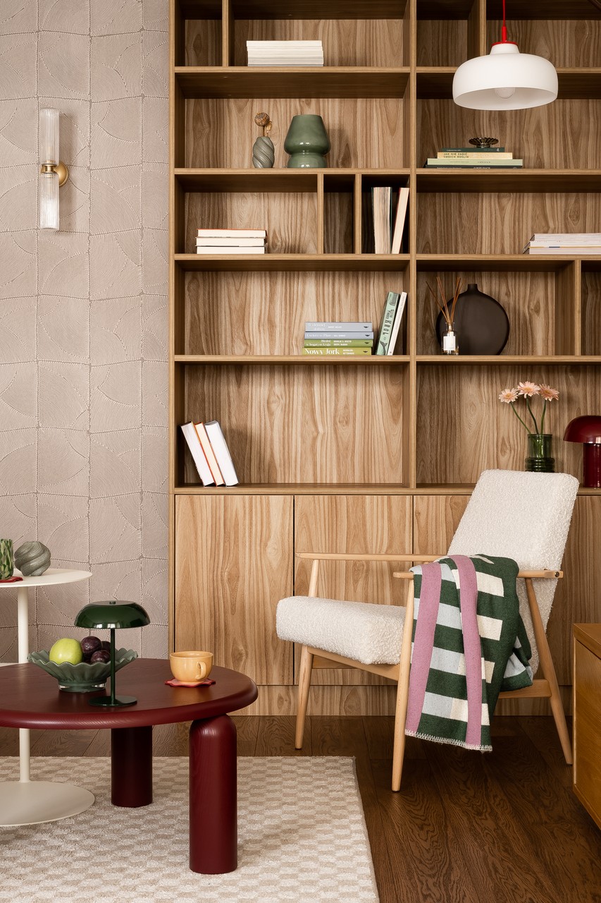 Przytulny kącik z designerskim fotelem i drewnianą biblioteczką.