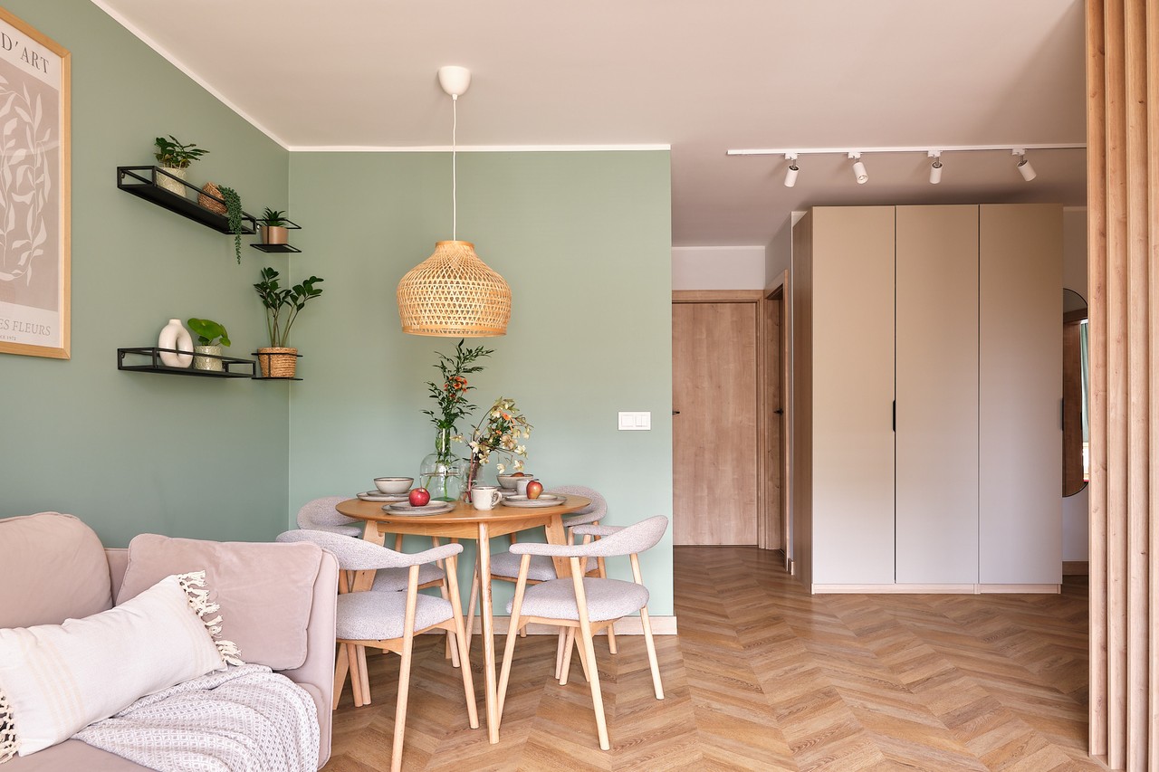 Salon z zieloną ścianą, drewnianymi krzesłami i elegancką lampą.