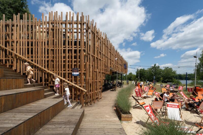 Drewniana architektura z tarasem i leżaki przy plaży.