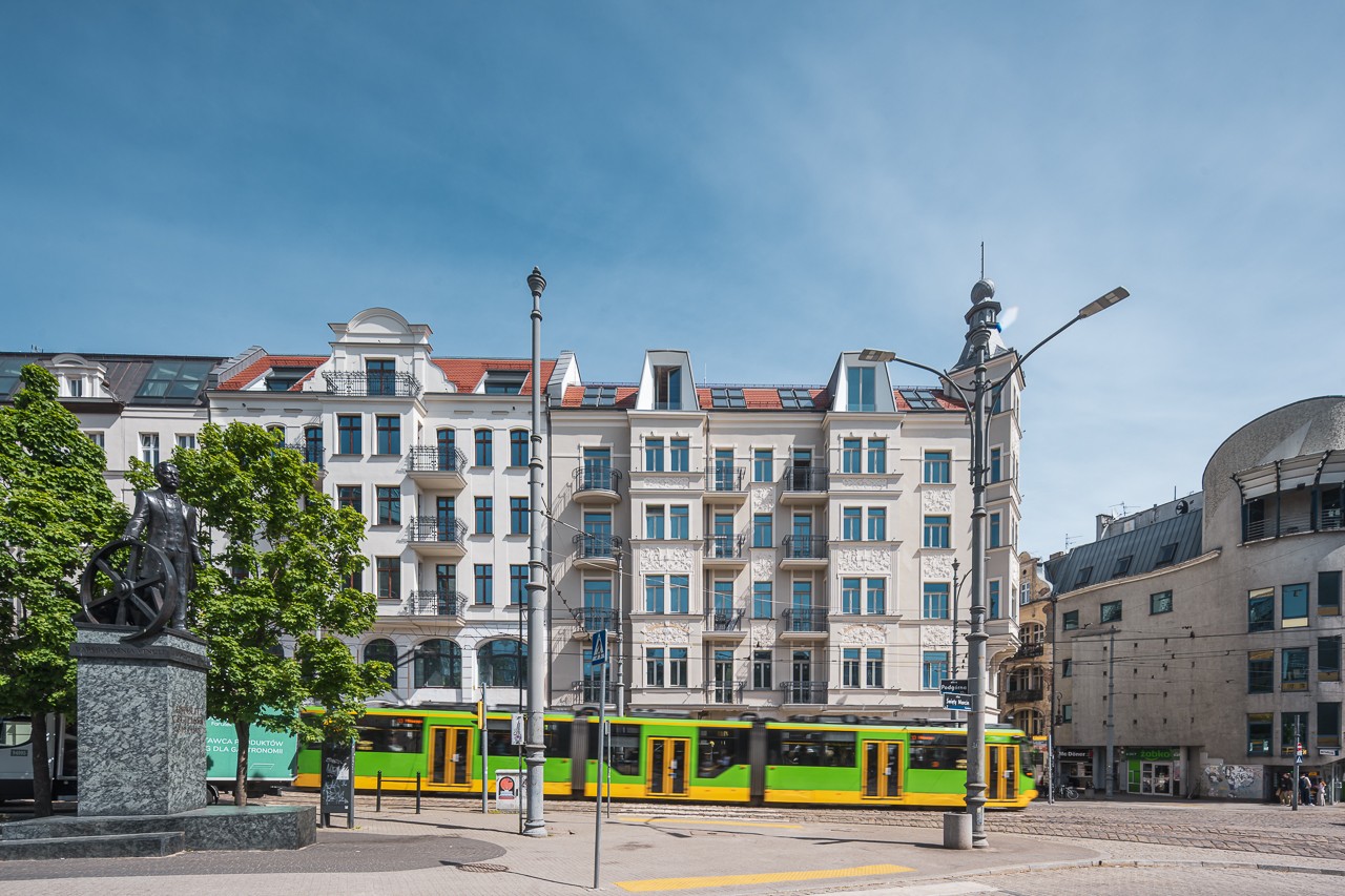 Klasyczna kamienica z eleganckimi balkonami i przejeżdżający tramwaj.