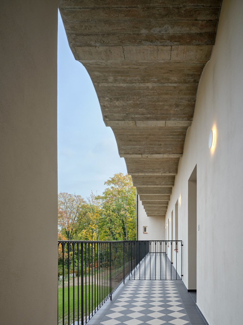 Balkon z płytek w szachownicę i betonowym sufitem.