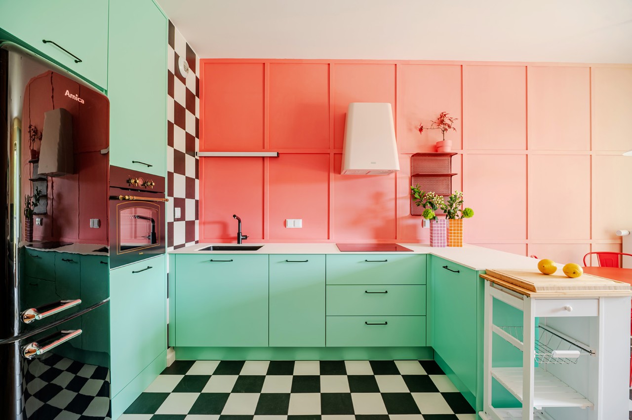 Kolorowa kuchnia z miętowymi szafkami i różową ścianą w stylu retro.