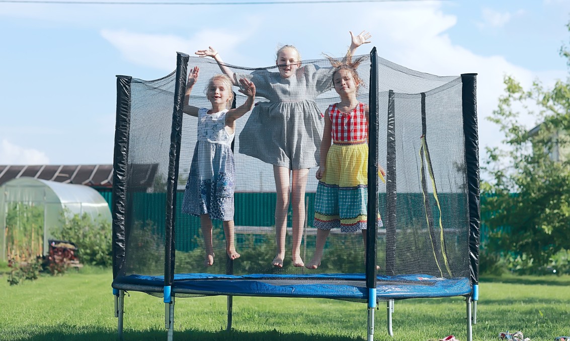 Dzieci bawią się na trampolinie w zielonym ogrodzie.