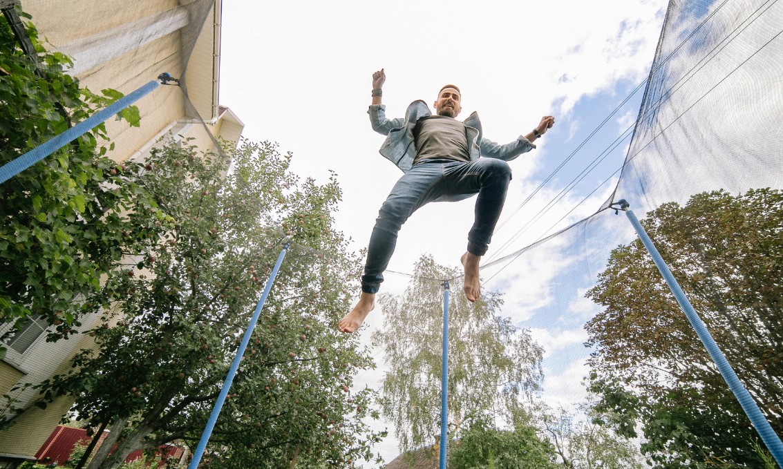 Skok na trampolinie, radość i ruch w otoczeniu drzew i budynku.
