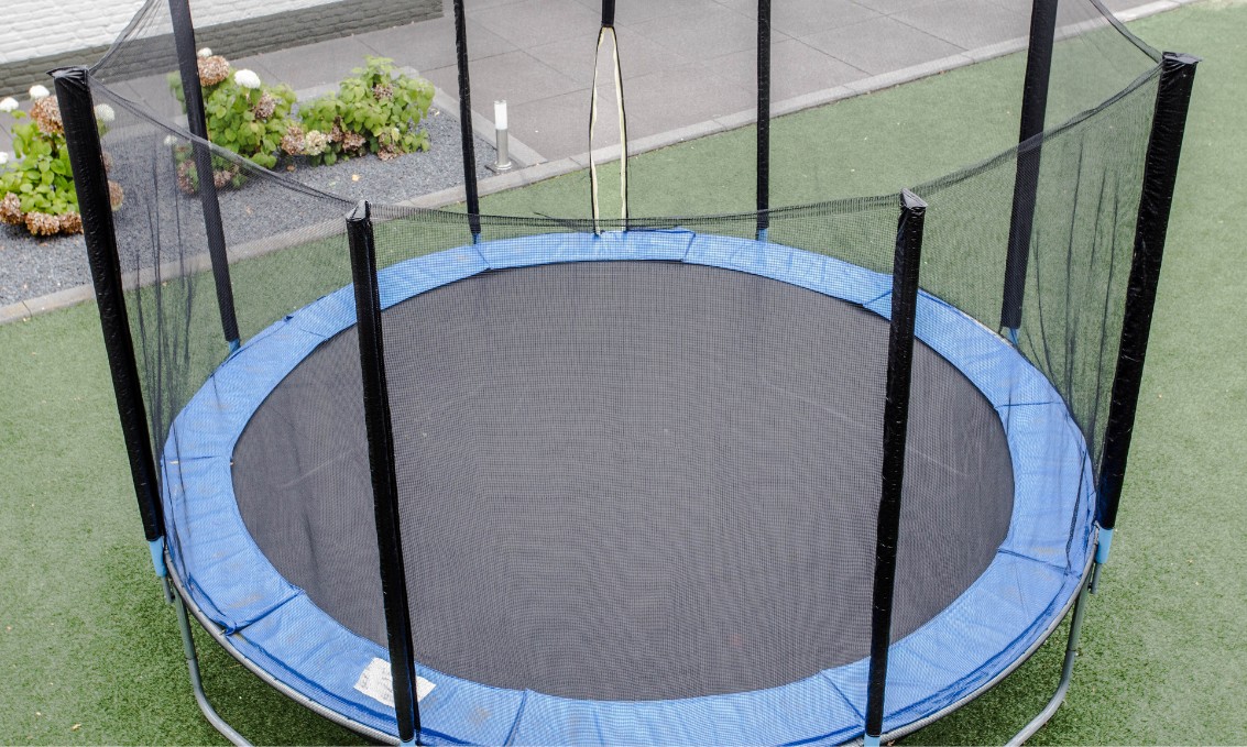 Duża trampolina ogrodowa z siatką bezpieczeństwa.
