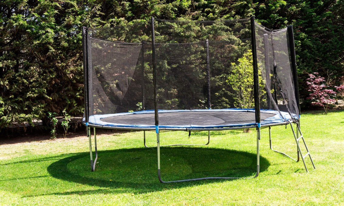 Trampolina ogrodowa wśród zieleni na słonecznej polanie.