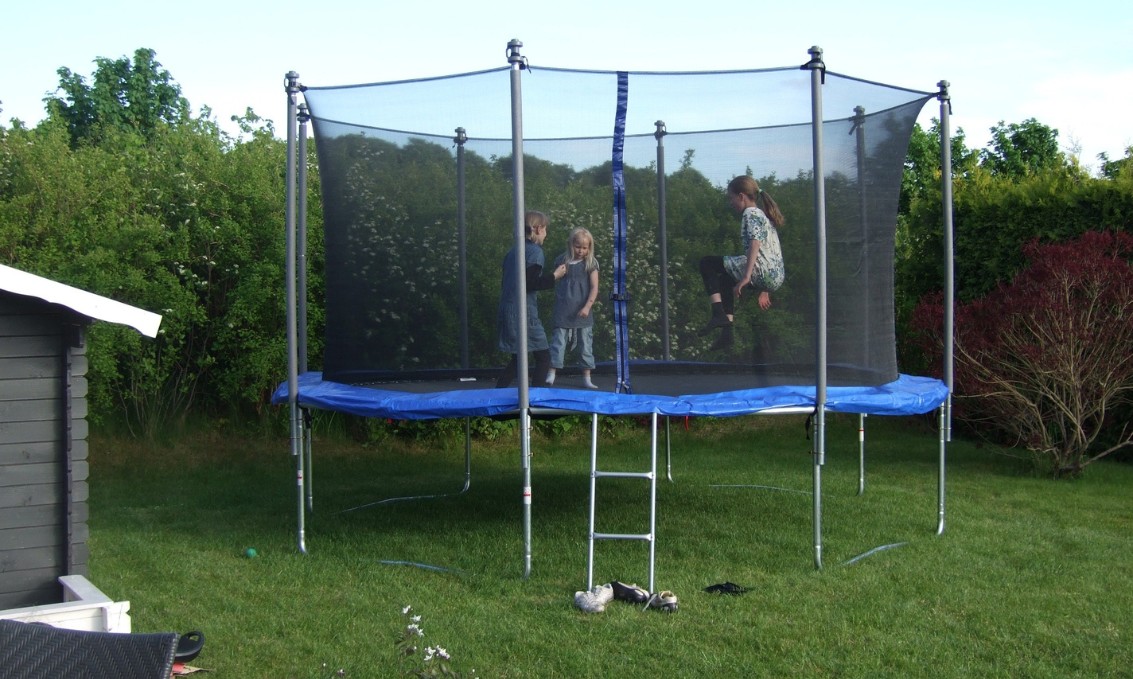 Dzieci bawiące się na trampolinie w ogrodzie pełnym zieleni.