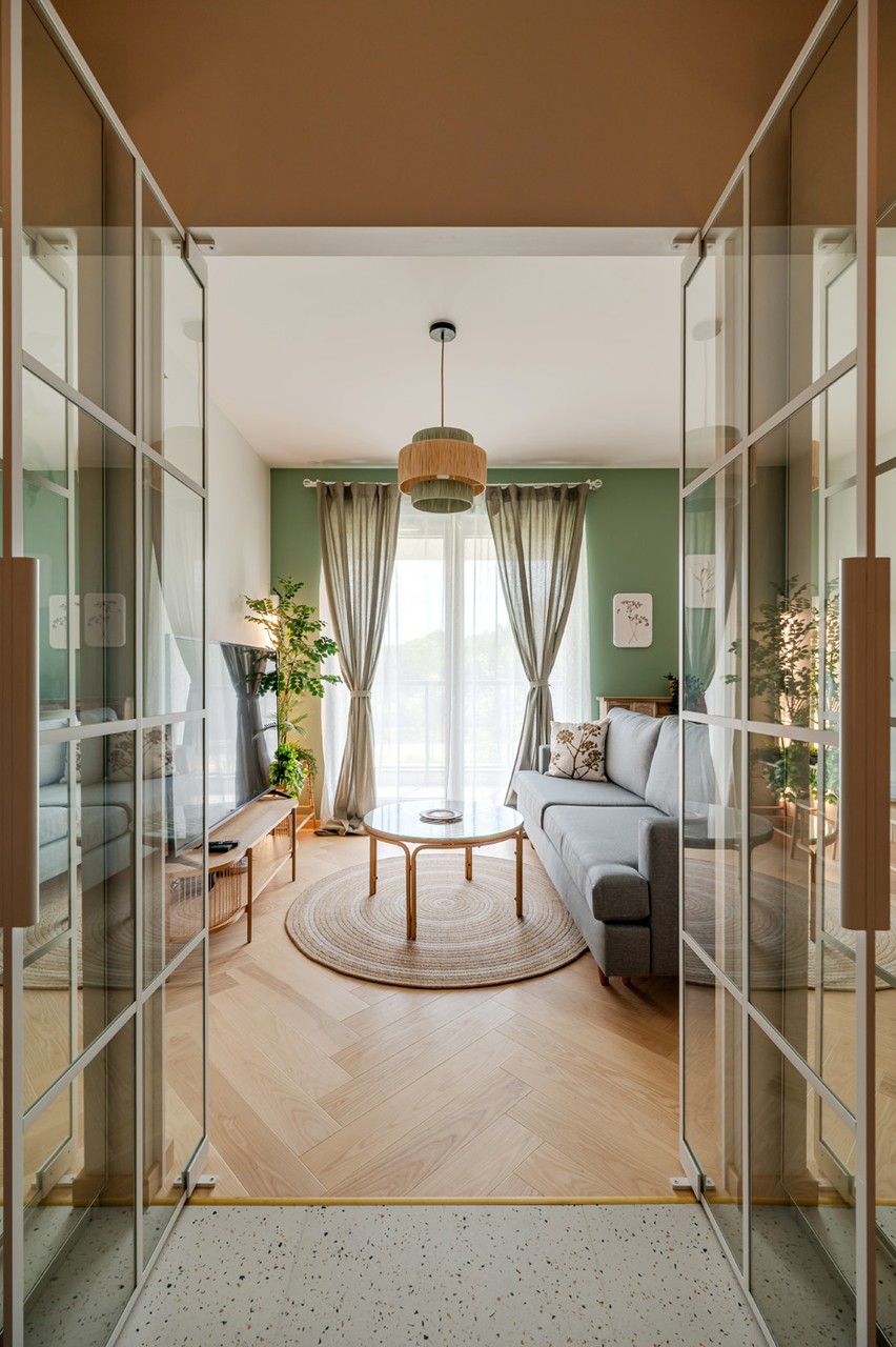 Przytulny salon z sofą, okrągłym stolikiem i zielonymi akcentami.