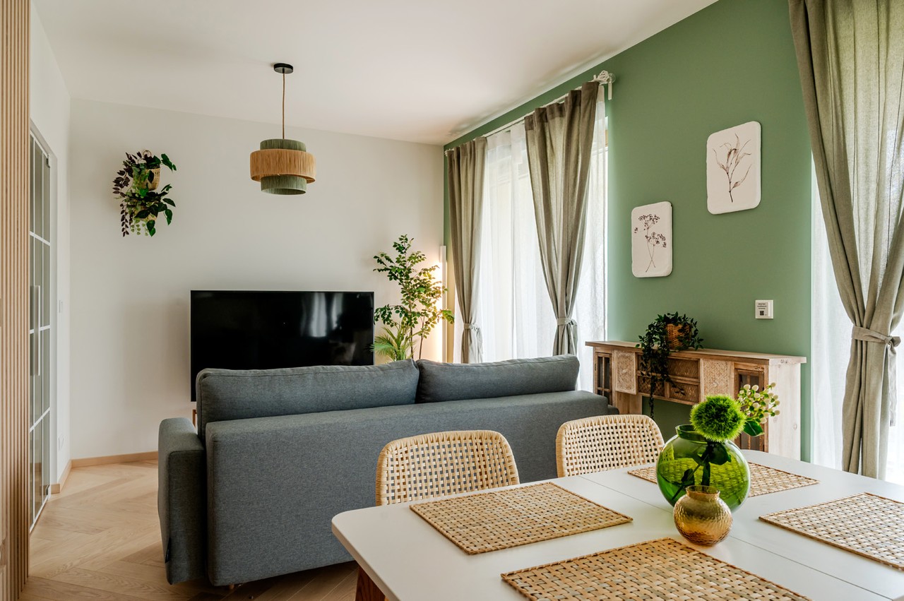 Przytulny salon z sofą, zielonymi akcentami i designerskim oświetleniem.