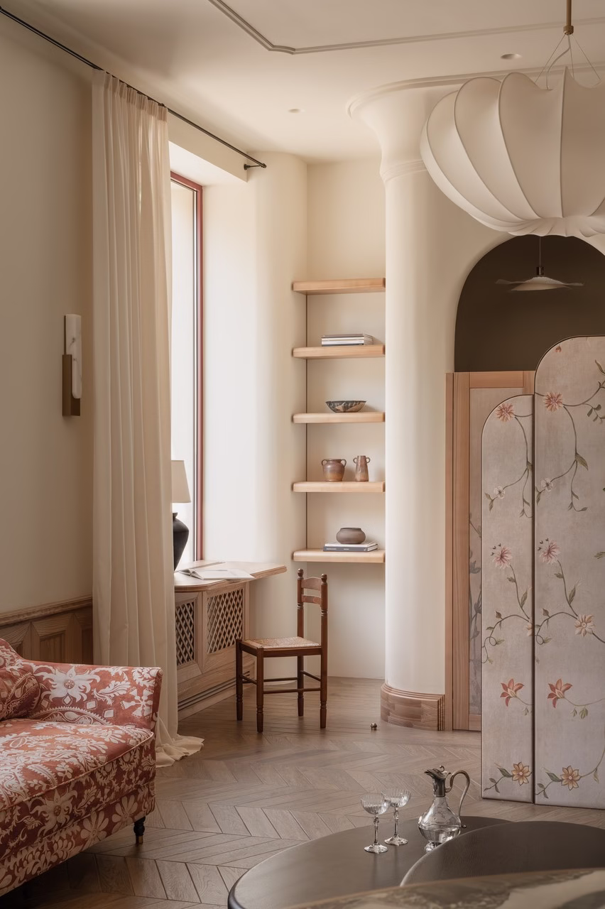 Elegancki salon z aksamitną sofą i florystycznym parawanem.