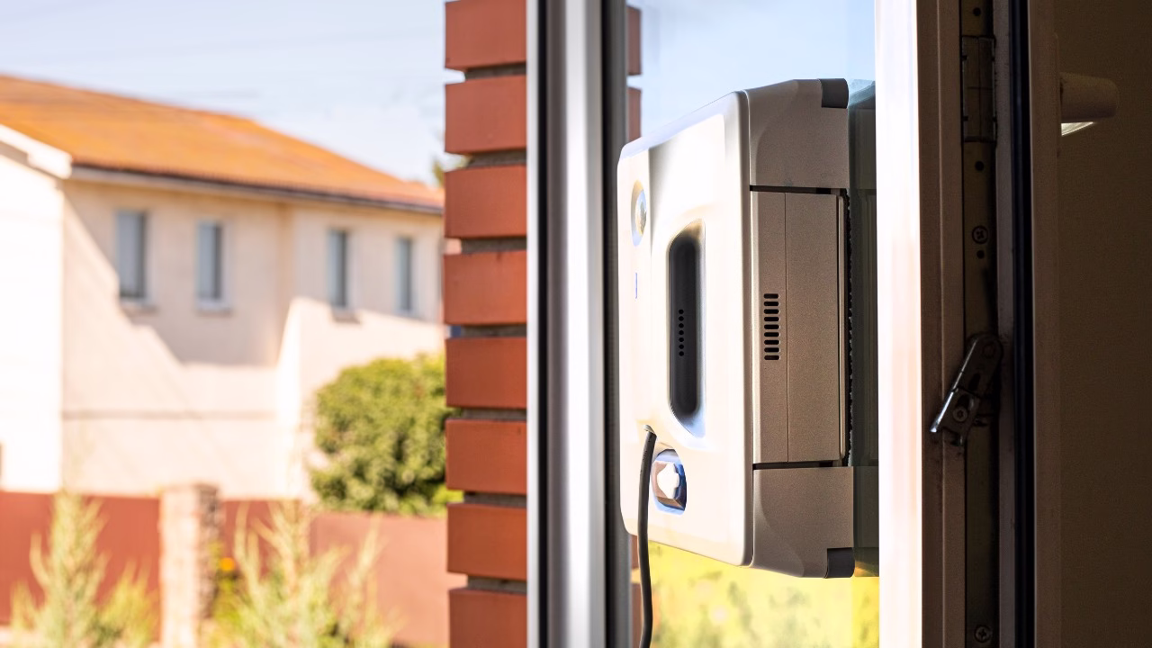 Robot myjący okno w nowoczesnym wnętrzu przy ceglanym murze.