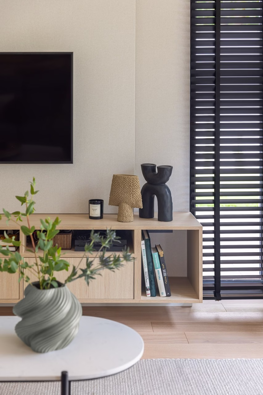 Minimalistyczny salon z designerskimi dodatkami i rośliną w wazonie.