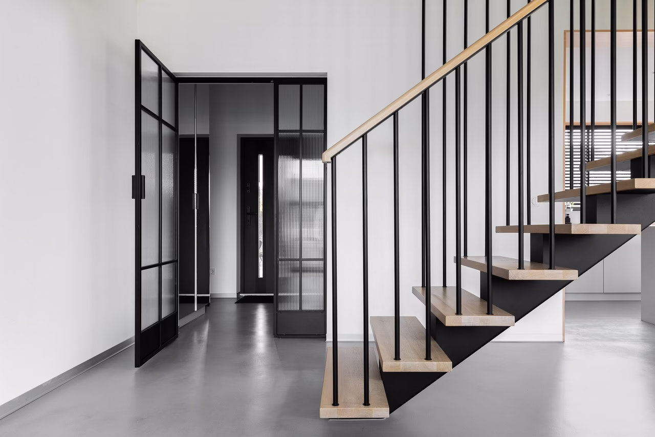 Nowoczesne schody drewniane z czarnymi balustradami i szklane drzwi.
