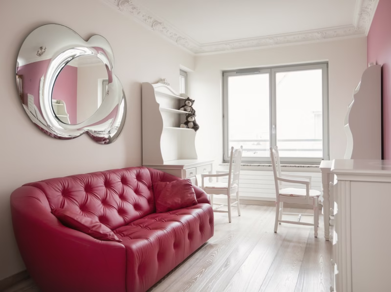 Czerwona sofa i designerskie lustro w jasnym, eleganckim wnętrzu.