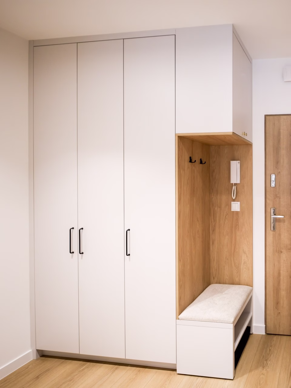 Minimalistyczna biała zabudowa wnękowa z drewnianymi akcentami i tapicerowaną ławką.