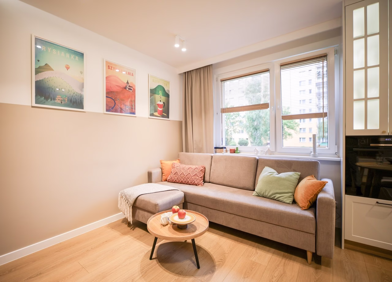 Nowoczesny salon z szarą kanapą, jasnymi ścianami i drewnianym stolikiem.