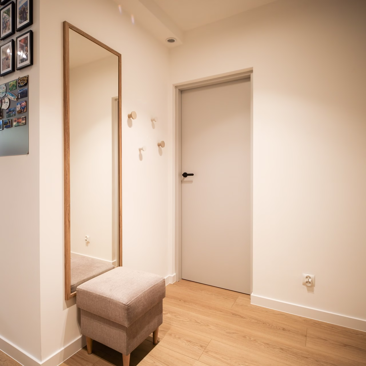 Korytarz minimalistyczny, jasne ściany, drewniana podłoga, duże lustro, pufa.