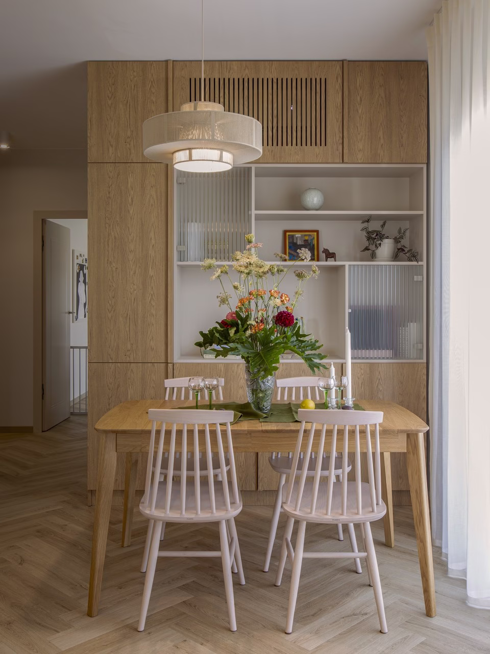Nowoczesna jadalnia z drewnianym stołem, kwiatami i białymi krzesłami.