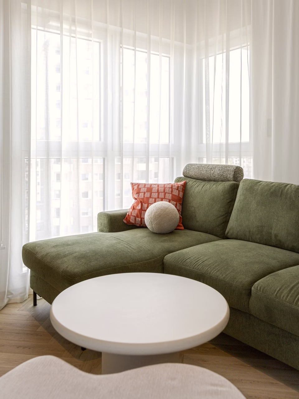 Elegancki salon z zieloną sofą, jasne zasłony, drewniana podłoga.