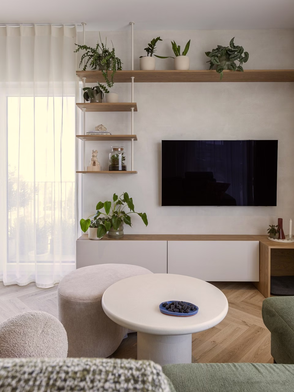 Nowoczesny salon z roślinami, minimalistycznymi półkami, zieloną kanapą i telewizorem.