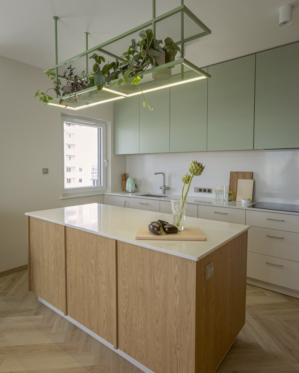 Nowoczesna kuchnia z drewnianą wyspą, miętowymi szafkami i roślinami pod sufitem.