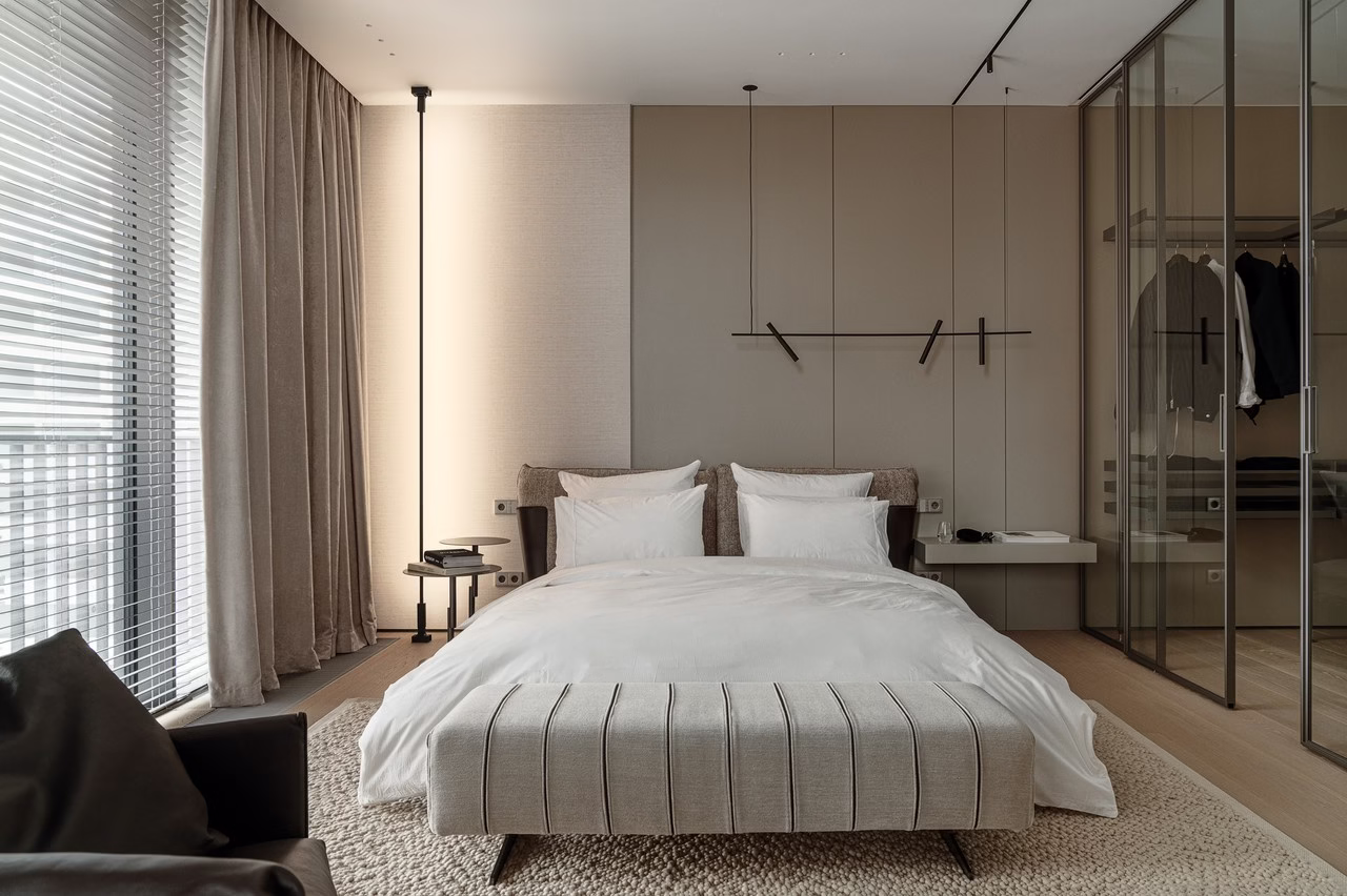 Nowoczesna sypialnia z beżowymi ścianami, szklanymi drzwiami i miękkim dywanem.